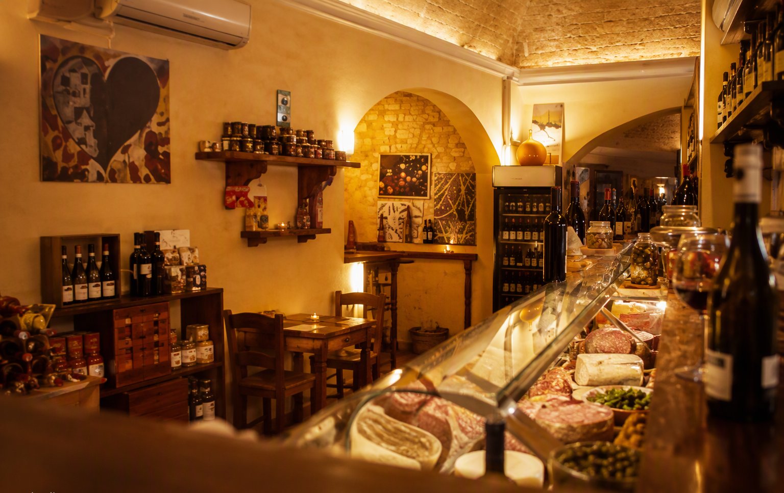 Il banco dell'enoteca con la vetrina dei salumi, gli scaffali dei vini e il murale